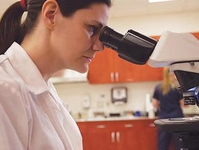 Pesquisadora observa uma amostra no microscópio