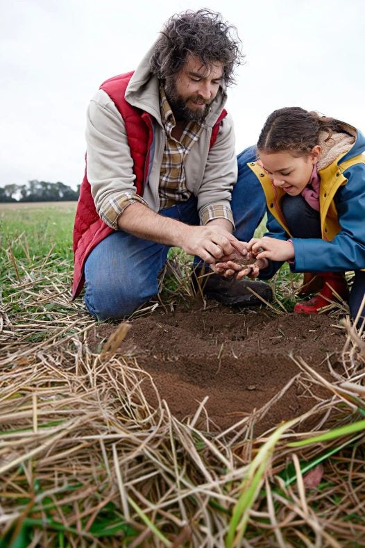 Produtor e menina observando a terra no campo